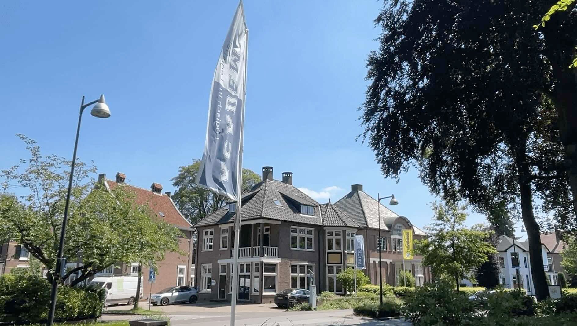 Beeld van het Bricklog-kantoor van buitenaf. De vlag van de Academie hangt voor het gebouw.